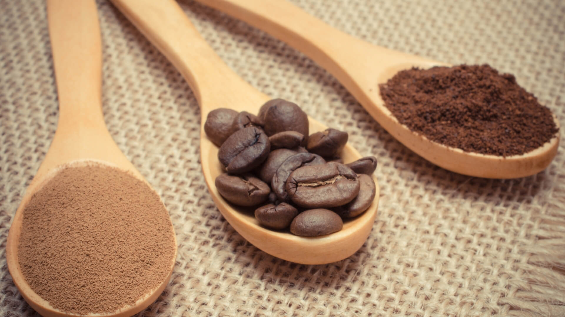 3 wooden spoons on the table presenting different types of coffee: coffee beans vs instant coffee vs ground coffee