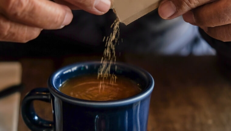 Man pouring brown sugar into his cup of fresh, hot coffee