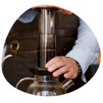 Barista making espresso with aeropress. He is pressing his hand on the top and the coffee pour to the pot