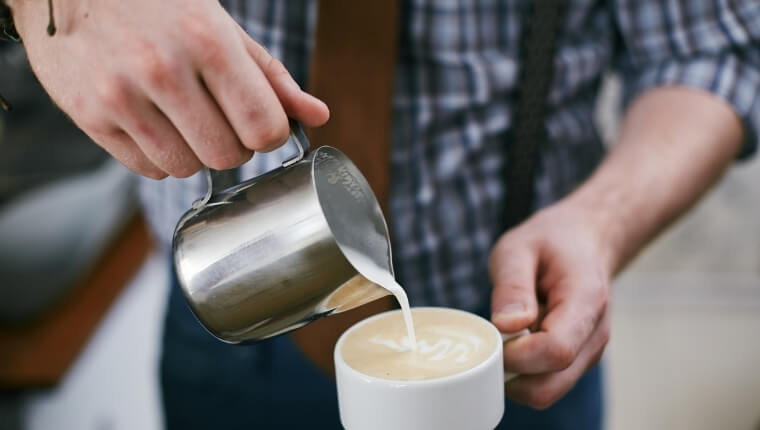 A man pouring freshly frothed milk into cup of latte