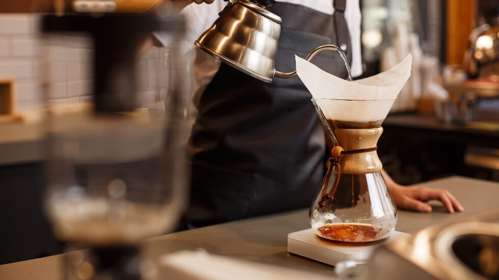 Professional barista making coffee using Chemex pour-over coffee maker and a goose kettle