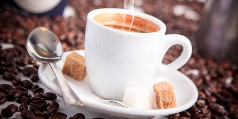 A traditional espresso cup called demitasse served on a small white plate with a spoon and brown sugar