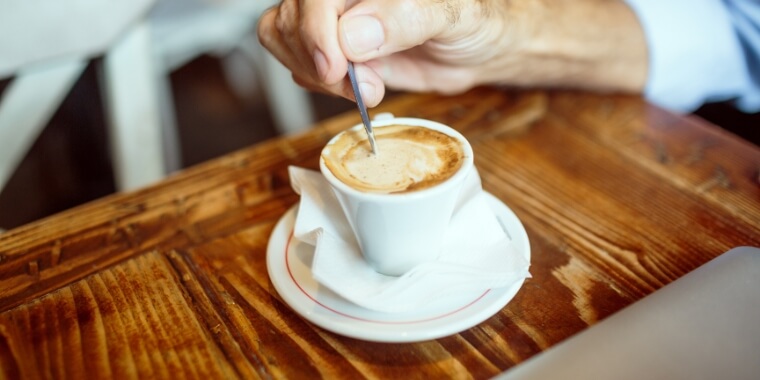 A man trying to fix bitter espresso by adding some sugar and giving it some stir