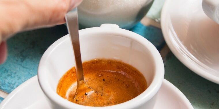 A hand stirring a freshly brewed espresso