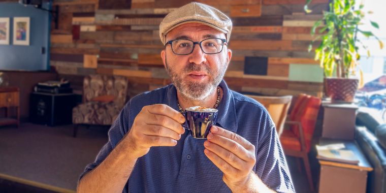 A man in a hat and glasses enjoying his espresso shot in the afternoon