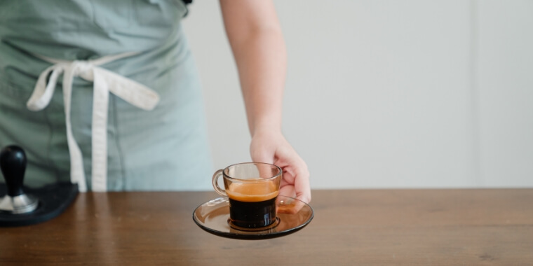 A woman serving an espresso on a cup